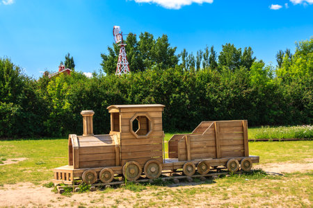 A wooden train is sitting in a field with a large windmill in the background. The train is a small model. The scene is peaceful and serene, with the trainの写真素材