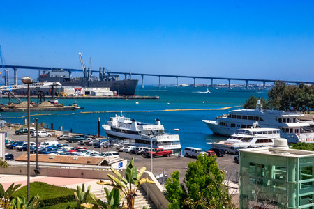 A large ship is docked at a pier next to a bridge. The pier is full of cars and boatsの写真素材