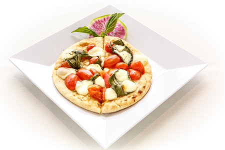 A slice of pizza with cheese and tomatoes on a white plate. The pizza is cut in half