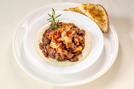 A plate of food with a piece of bread on the side. The food is a stew with meat and vegetablesの写真素材