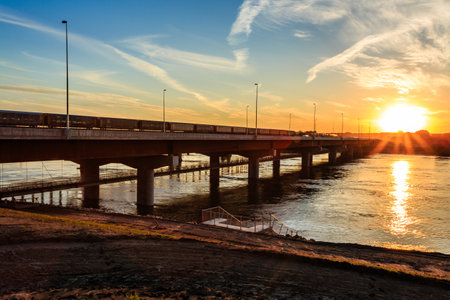 A bridge over a river with a sunset in the background. The bridge is illuminated by the sun, creating a warm and peaceful atmosphereの写真素材