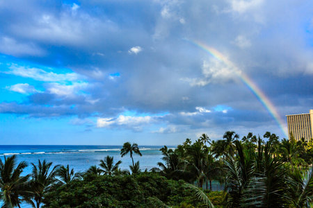 A rainbow is seen in the sky above a beach. The sky is cloudy and the ocean is in the backgroundの写真素材
