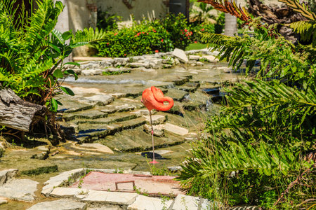 A pink flamingo is standing in a garden with a stone path. The flamingo is the main focus of the image, and the garden setting creates a peaceful and serene atmosphereの写真素材