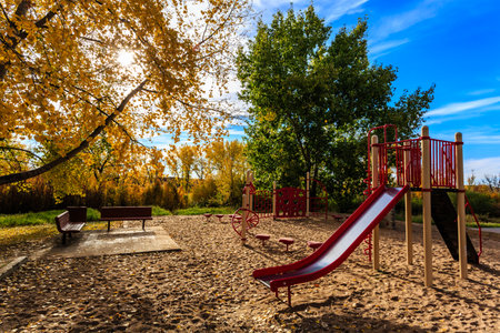 A playground with a red slide and a bench. The playground is empty and the sun is shiningの写真素材