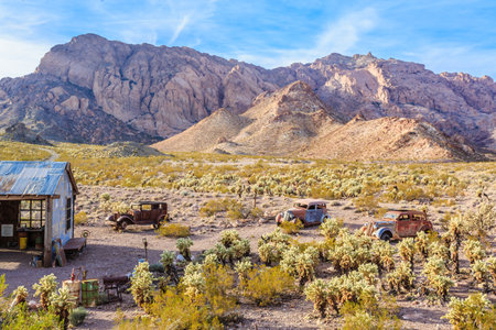 A desert landscape with a small cabin and a few old cars. The scene is peaceful and serene, with the mountains in the background adding to the sense of isolation and tranquilityの写真素材