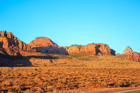 A desert landscape with a mountain in the background. The sky is clear and blue. The sun is setting, casting a warm glow over the sceneの写真素材