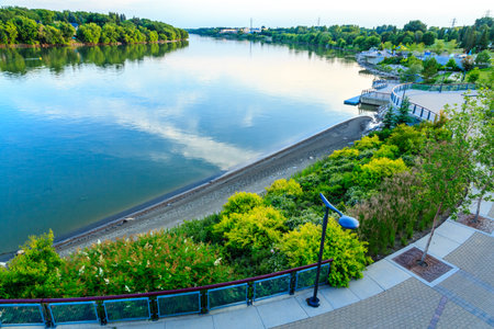A beautiful view of a river with a green hillside and a park. The water is calm and the sky is cloudyの写真素材