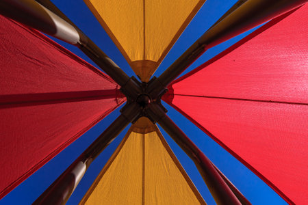 A colorful umbrella with a blue sky in the background. The umbrella is red, yellow, and orangeの写真素材