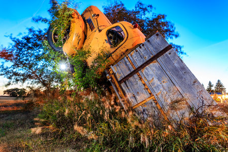 A yellow school bus has crashed into a wooden fence. The bus is upside down and the fence is broken. The scene is eerie and unsettlingの写真素材