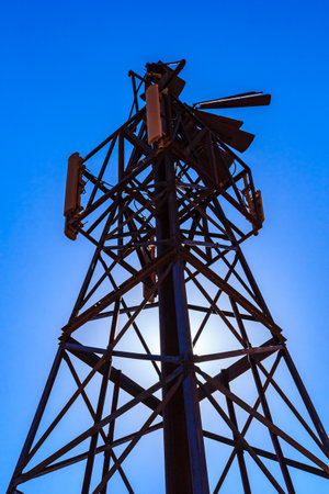 A tall metal tower with a windmill on top. The tower is surrounded by a lot of wires and is located...