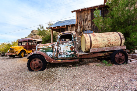 An old truck is parked in front of a house. The truck is covered in rust and has a green top. The...