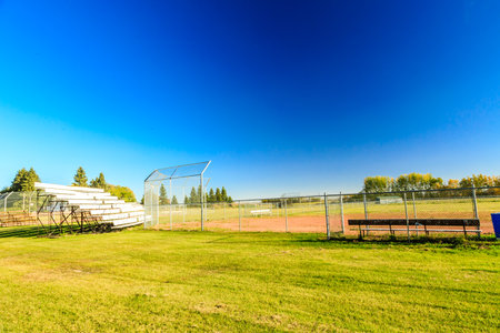 A baseball field with a fence and bleachers. The sky is blue and clear. The field is emptyの写真素材