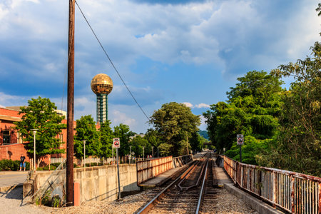 A train track with a bridge over it and a tall building in the background. The sky is cloudy and the atmosphere is somewhat gloomyの写真素材