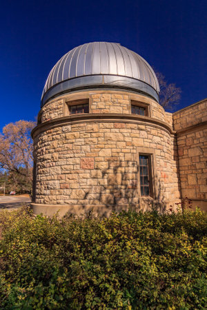 A large building with a dome on top. The dome is made of metal and is on the side of the building. The building is surrounded by bushes and treesの写真素材