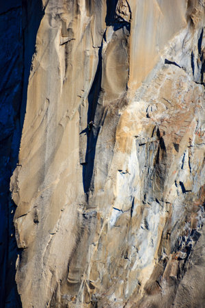A rock wall with a lot of cracks and crevices. The wall is made of sandstone and has a rough texture. The sun is shining on the wall, making it look warmの写真素材
