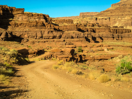 A dirt road winds through a rocky canyon. The road is narrow and winding, and the canyon is full of rocks and boulders. The sky is clear and blue, and the sun is shining brightlyの写真素材