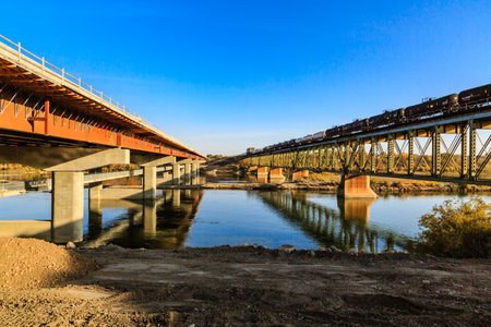Two bridges over a river with a blue sky in the background. The bridge on the left is a concrete one and the one on the right is a metal oneの写真素材