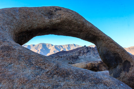 A large rock with a hole in it, with mountains in the background. The rock is a natural arch, and the mountains are in the distance. The scene is peaceful and sereneの写真素材