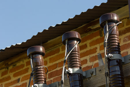 Three brown poles with black caps are on a roof. The poles are connected to wires and are likely part of an electrical system. The image has a somewhat industrial or technical feel to itの写真素材