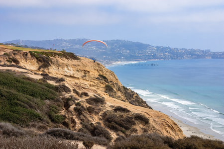 A man is flying a kite on a beach near a cliff. The sky is clear and the ocean is calmの写真素材