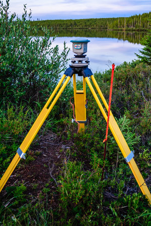 A yellow tripod is set up in a field next to a body of water. The tripod is being used to take...