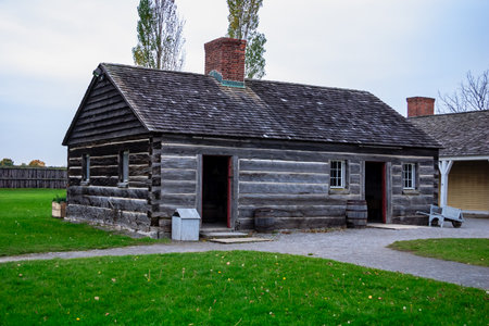 A small log cabin with a chimney and a porch. The building is surrounded by a grassy areaの写真素材