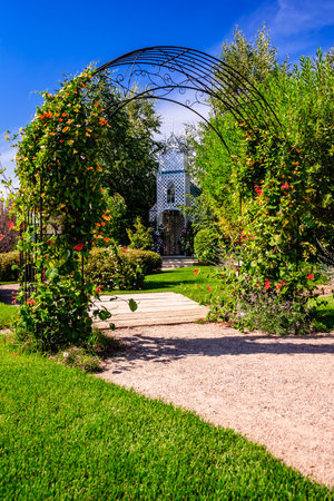 A garden with a stone path and a metal archway. The archway is covered in vines and flowersの写真素材
