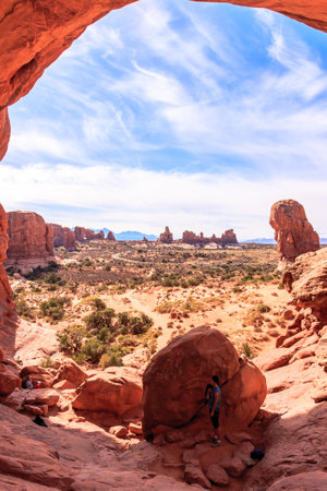 A person is climbing a rock in a desert. The desert is full of rocks and the sky is blueの写真素材