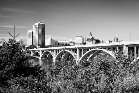A bridge spans a river in a city. The bridge is surrounded by trees and buildings. The sky is clear and the sun is shiningの写真素材