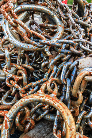 A pile of rusty chains with a few of them having a silver ring. The chains are old and rusted,...