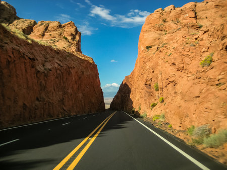 A road with a canyon in the background. The road is empty and the sky is blue. The road is a two way road with a yellow line down the middleの写真素材