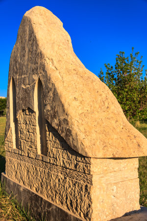 A large stone headstone with a slanted top. The stone is brown and has a weathered look. The sky is blue and clear, and there are trees in the backgroundの写真素材