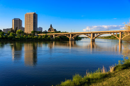 A bridge spans a river with a city in the background. The sky is clear and blue, and the water is calmの写真素材