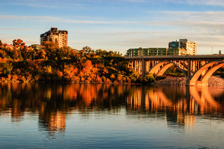 A bridge spans a river with a city in the background. The water is calm and the sky is a beautiful shade of blueの写真素材