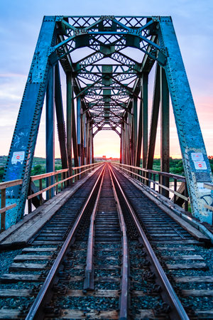 A bridge with train tracks and a sunset in the background. The bridge is old and has graffiti on itの写真素材