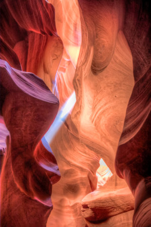 A narrow canyon with a red and white color scheme. The canyon is carved out of a rock, and the walls are steep and jagged. The sunlight is shining through the canyon, creating a warmの写真素材
