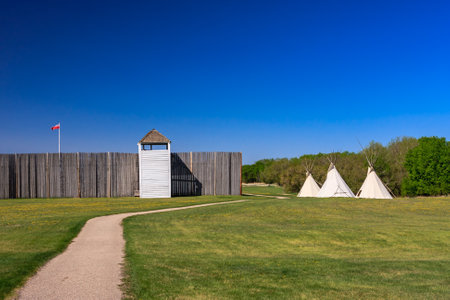 A path leads to a building with a white roof and a red flag on a pole. The flag is on the left side of the building. The grass is green and the sky is blueの写真素材