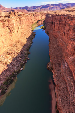 A river runs through a canyon with a rocky shoreline. The water is clear and calm. The canyon is surrounded by mountains, and the sky is blueの写真素材