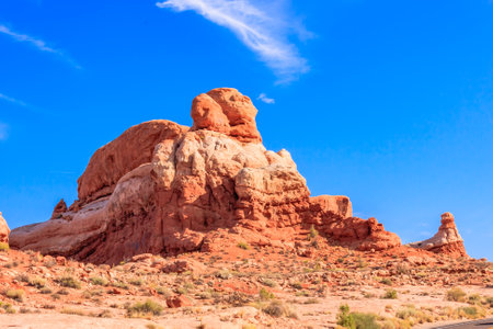 A large rock formation sits in the desert with a clear blue sky above it. The rock formation is a large, jagged, and rocky hill with a few smaller rocks scattered around itの写真素材