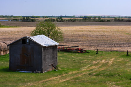 A small, old, and rusted barn sits in a field. The barn is surrounded by a large, empty fieldの写真素材
