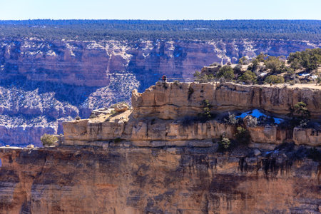 A mountain range with a blue sky in the background. The mountain range is rocky and has a cliff that is partially covered in snowの写真素材