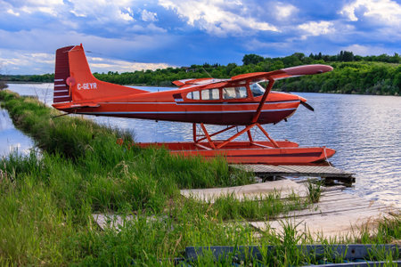 A red plane is sitting on a grassy area next to a body of water.