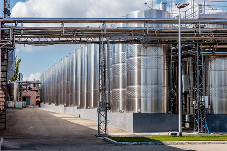 A large industrial plant with many tanks and pipes. The tanks are silver and the pipes are metal. Scene is industrial and mechanicalの写真素材