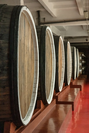 A row of barrels with a red floor in the background. The barrels are wooden and have a white stripeの写真素材