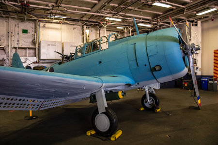 A blue airplane is parked in a hangar. The plane is old and has a vintage look. The hangar is dimly...