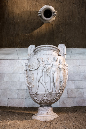 A white vase with a woman on it sits on a stone floor. The vase is decorated with a woman and two other figures. The scene is quiet and peaceful, with the vase as the main focusの写真素材