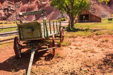 An old wagon is parked in front of a barn. The wagon is green and has a wooden frame. The barn is old and has a rustic appearance. The scene is peaceful and quietの写真素材