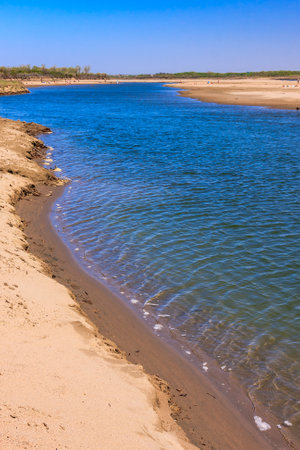 A river with a sandy beach on the shore. The water is calm and clear. The sky is blue and there are no cloudsの写真素材