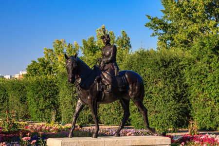A statue of a woman riding a horse in a park. The statue is black and the woman is wearing a dress. The park is filled with trees and flowers, creating a peaceful and serene atmosphereの写真素材