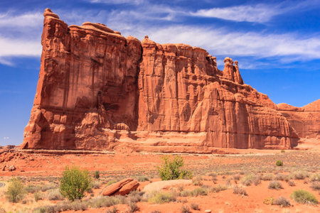 A large rock formation with a few trees in the foreground. The sky is blue and the sun is shiningの写真素材